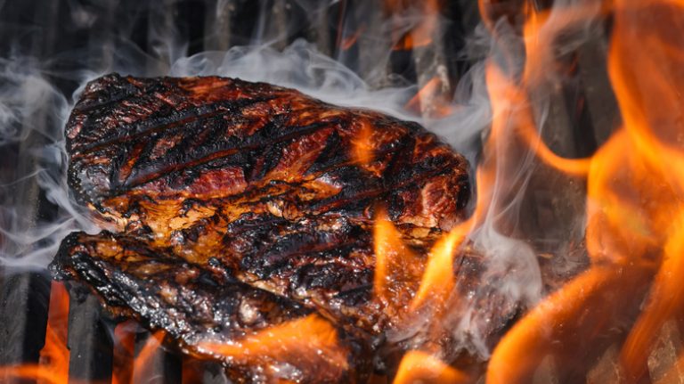 Charred steak on firey grill